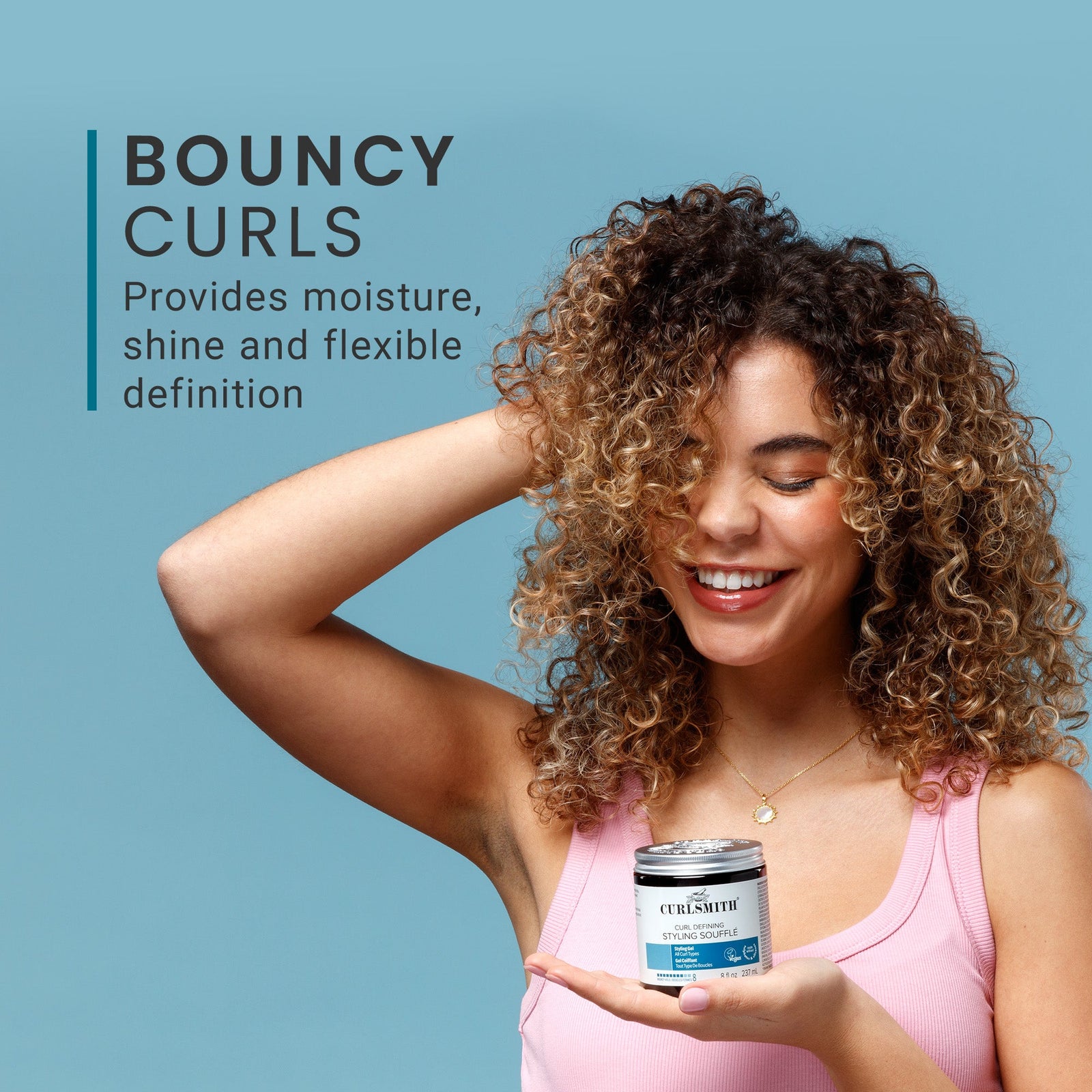 Woman with curly hair holding a Curl Defining Styling Souffle container against a blue background