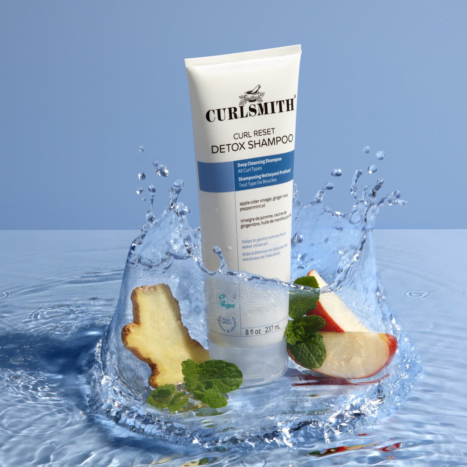 Curlsmith Curl Reset Detox Shampoo with apple slices and ginger on a water splash background