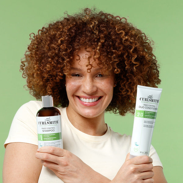 Woman holding Curlsmith Frizz Control hair care products against a green background