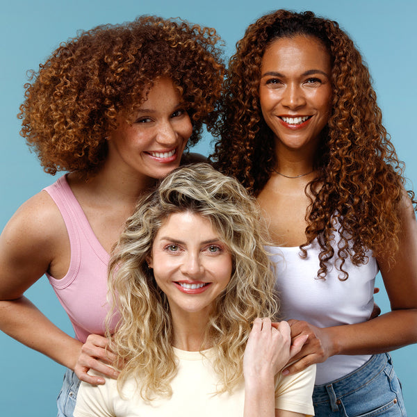 Three women with curly hair smiling against a blue background