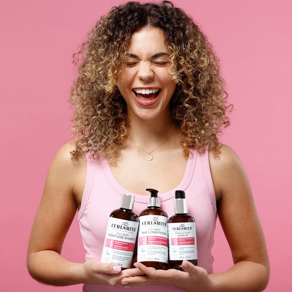 Woman holding Curlsmith Volume hair care products against a pink background
