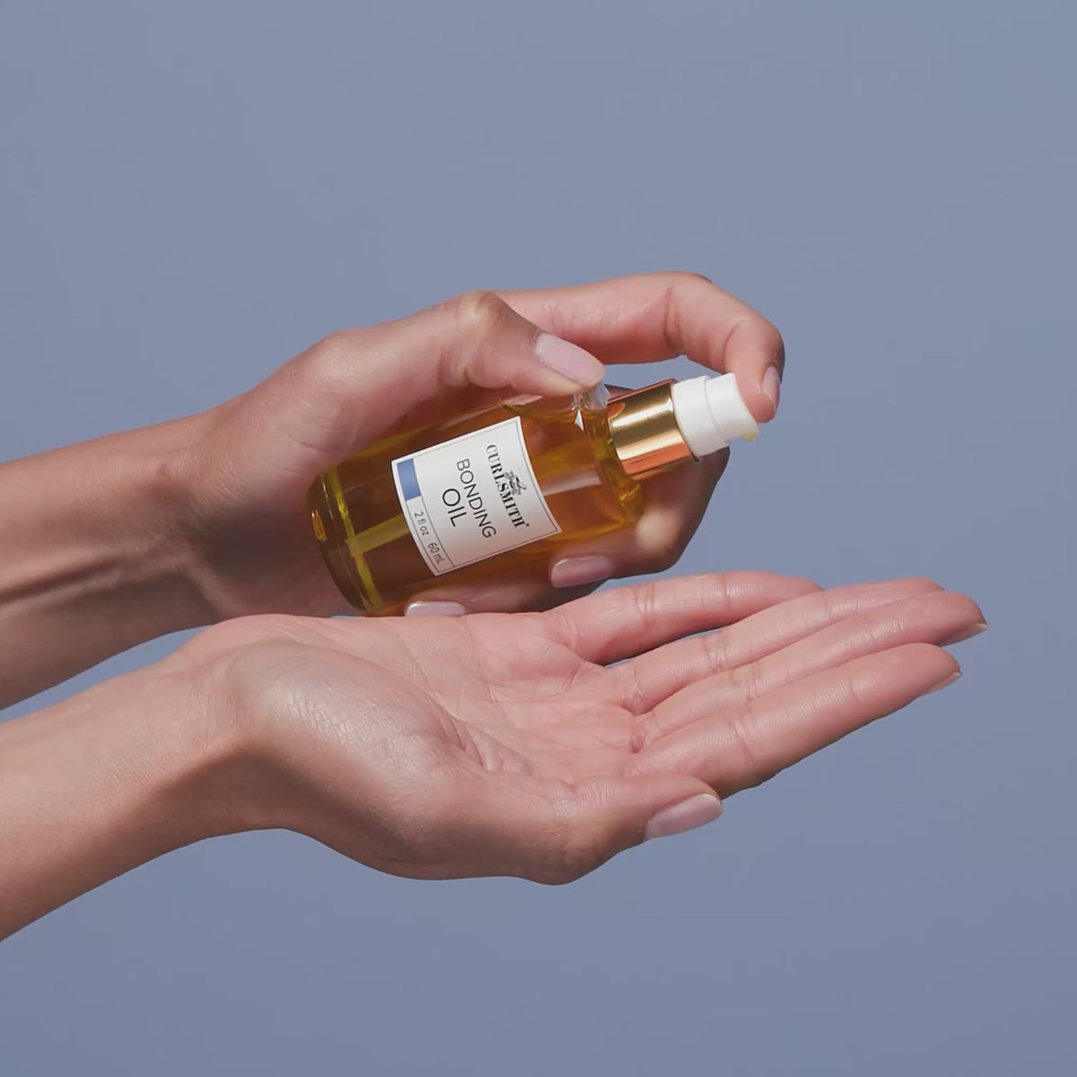 Hands holding a bottle of Bonding oil for curly hair
