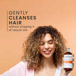 Woman holding a bottle of Curlsmith Curl quenching conditioning wash hair care product with text on a beige background
