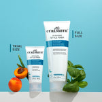 Two sized bottles of Curlsmith In-Shower Style Fixer with a peach and basil leaf on a blue background