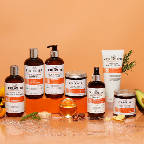 Collection of Curlsmith moisture hair care products on a wooden surface with an orange background