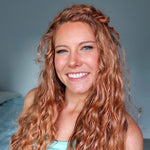 Woman with long, wavy red hair smiling against a neutral background