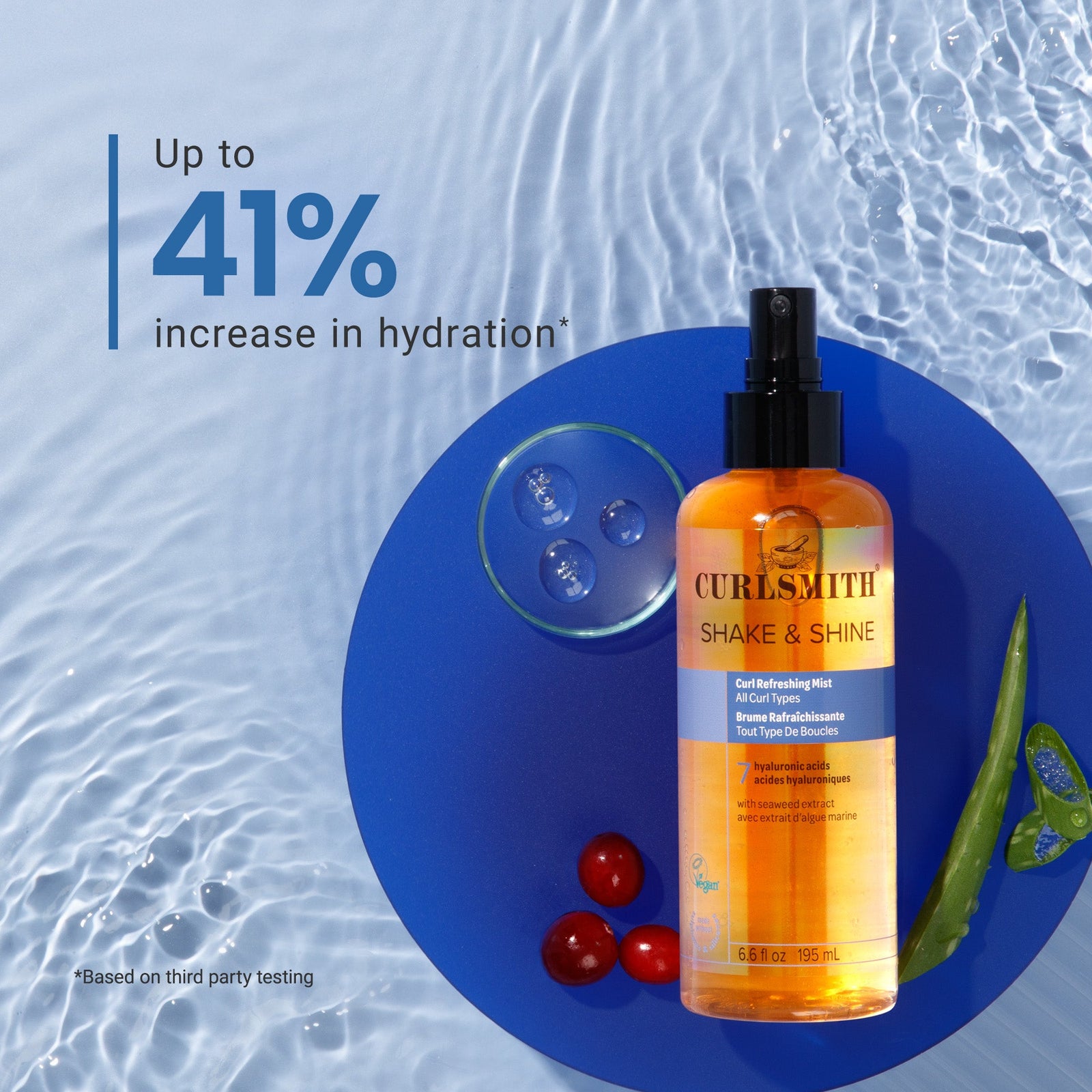 Curlsmith Shake & Shine product on a blue circular mat with water droplets and cherry tomatoes.