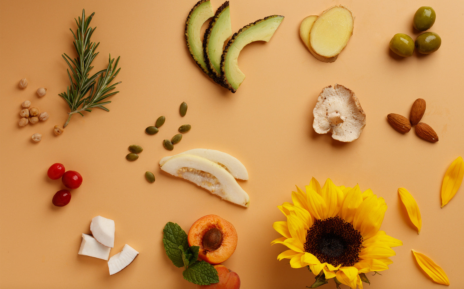 Arrangement of ingredients such as fruits, vegetables, and a sunflower on a beige background