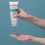 Hand squeezing In-shower style fixer gel tube on hand with blue background
