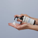 Hand pumping Fragrance-Free Conditioner in hand below on a bright blue background