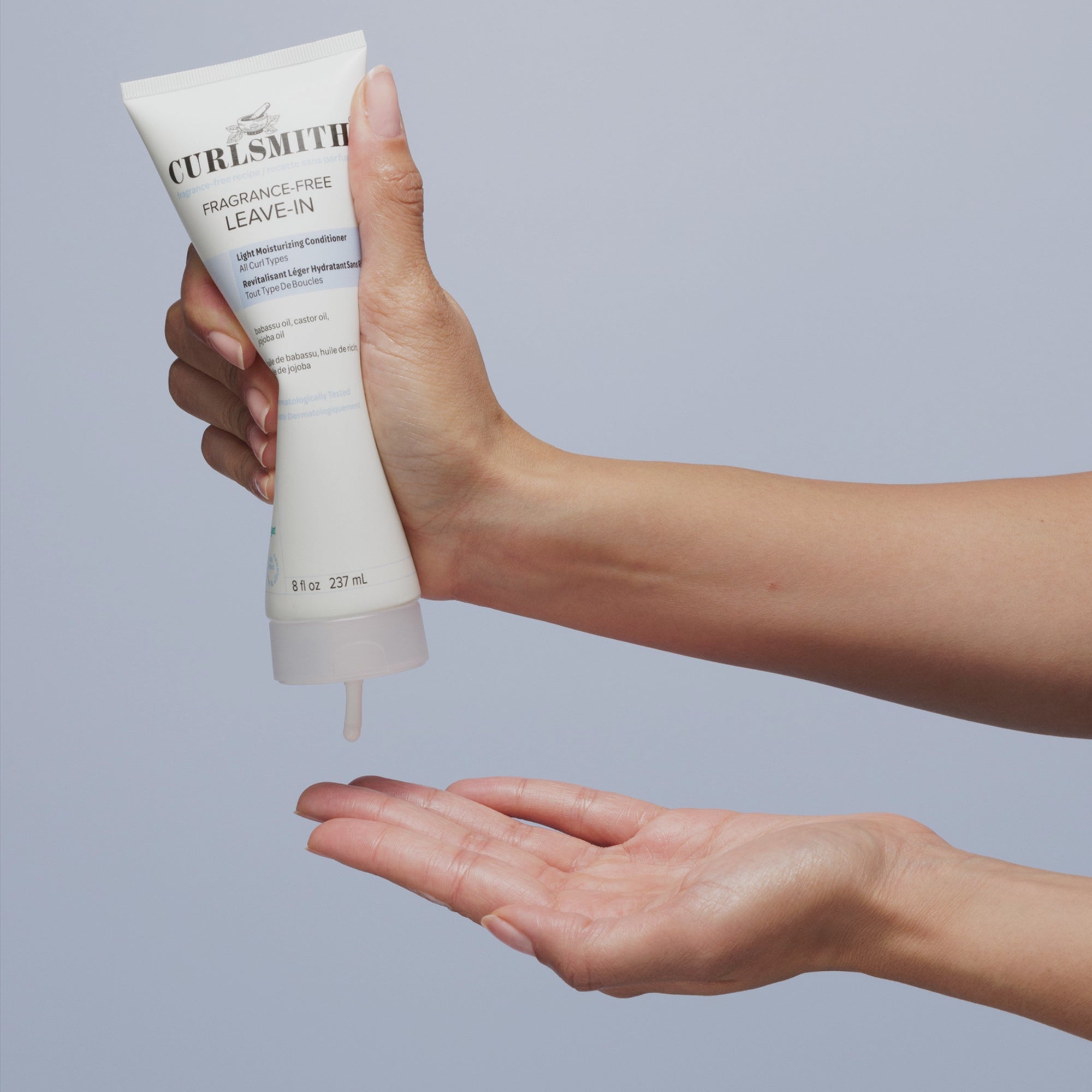 Hand squeezing Fragrance-Free Leave-in on hand below on a bright blue background