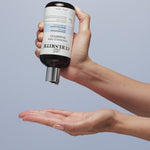 Hand holding Fragrance-Free Shampoo dropping it in hand below on a bright blue background