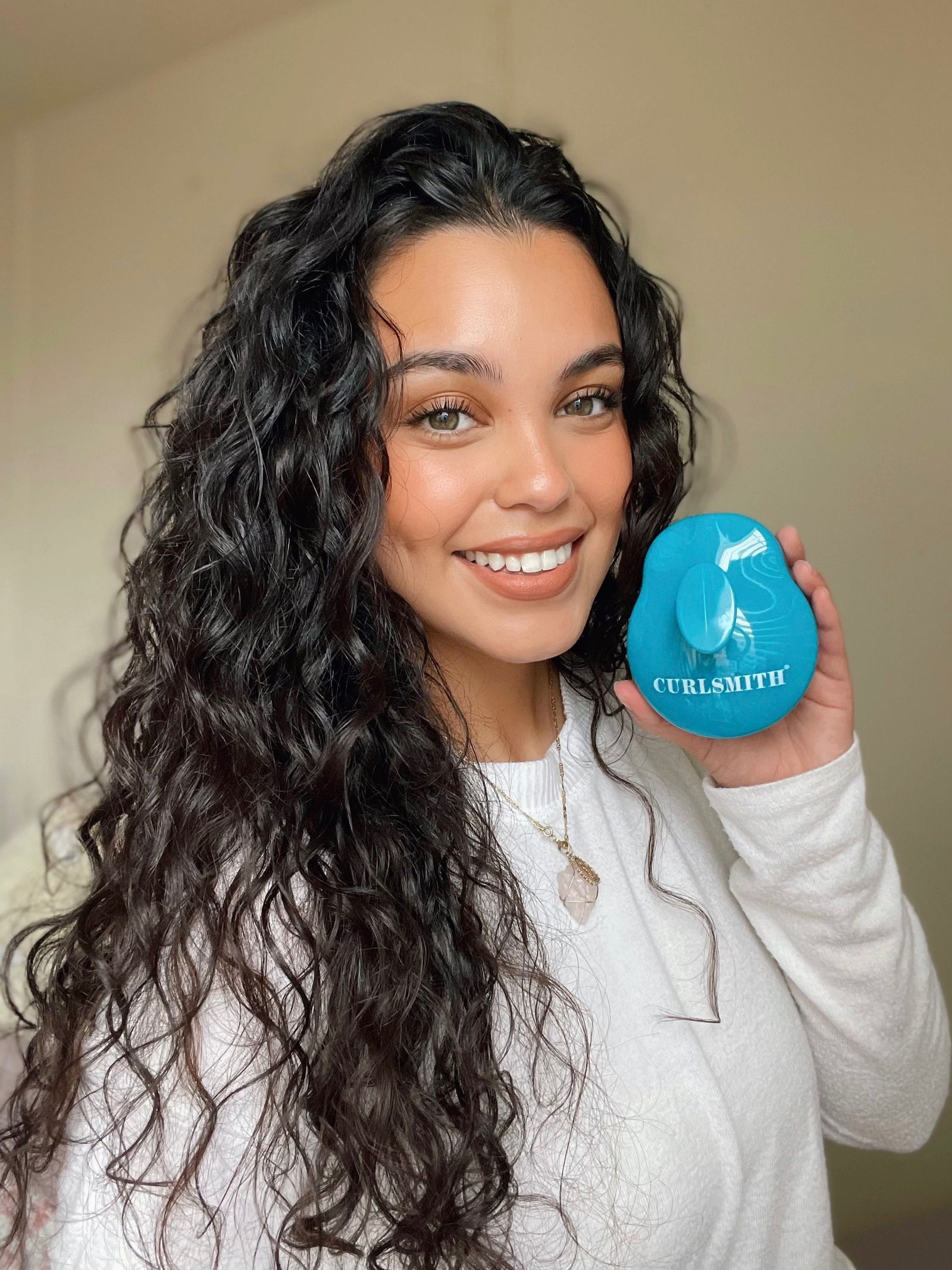 Woman holding a blue scalp massager with the brand name Curlsmith inscribed on it.