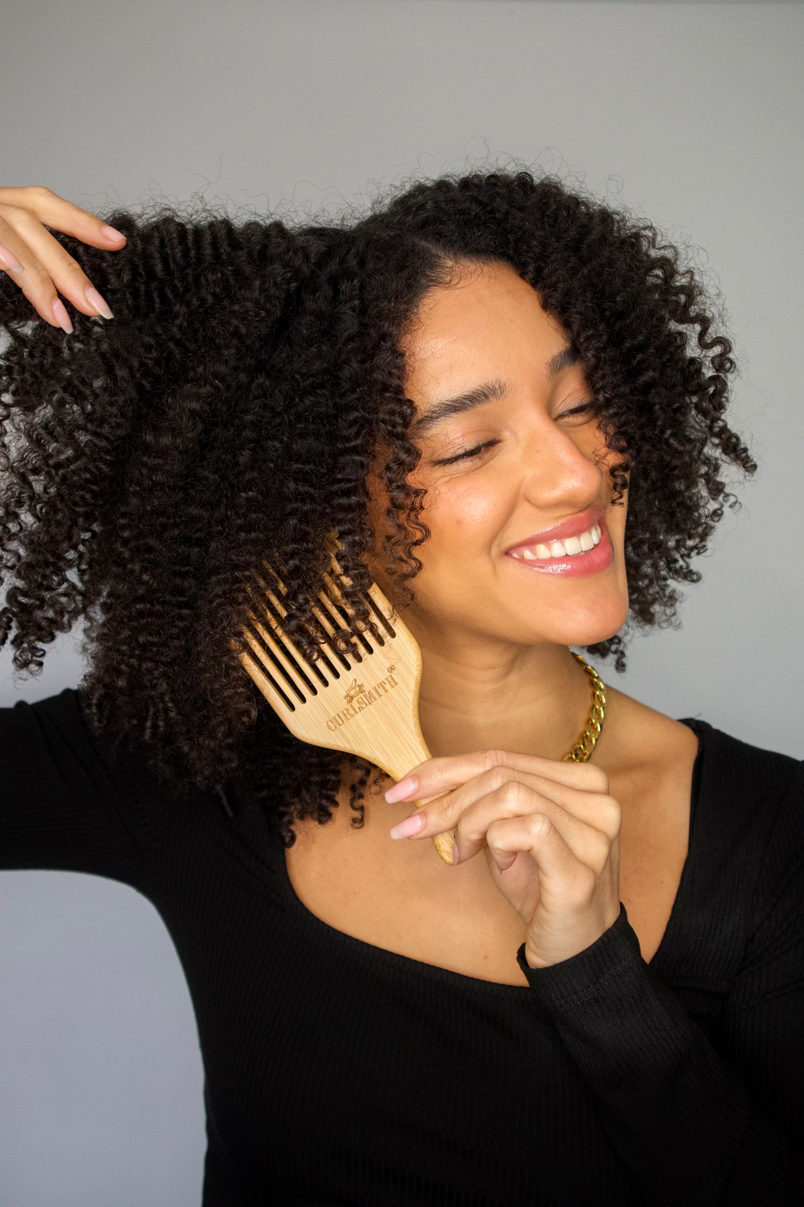 Woman holding a bamboo hair pick with a wide-tooth design.