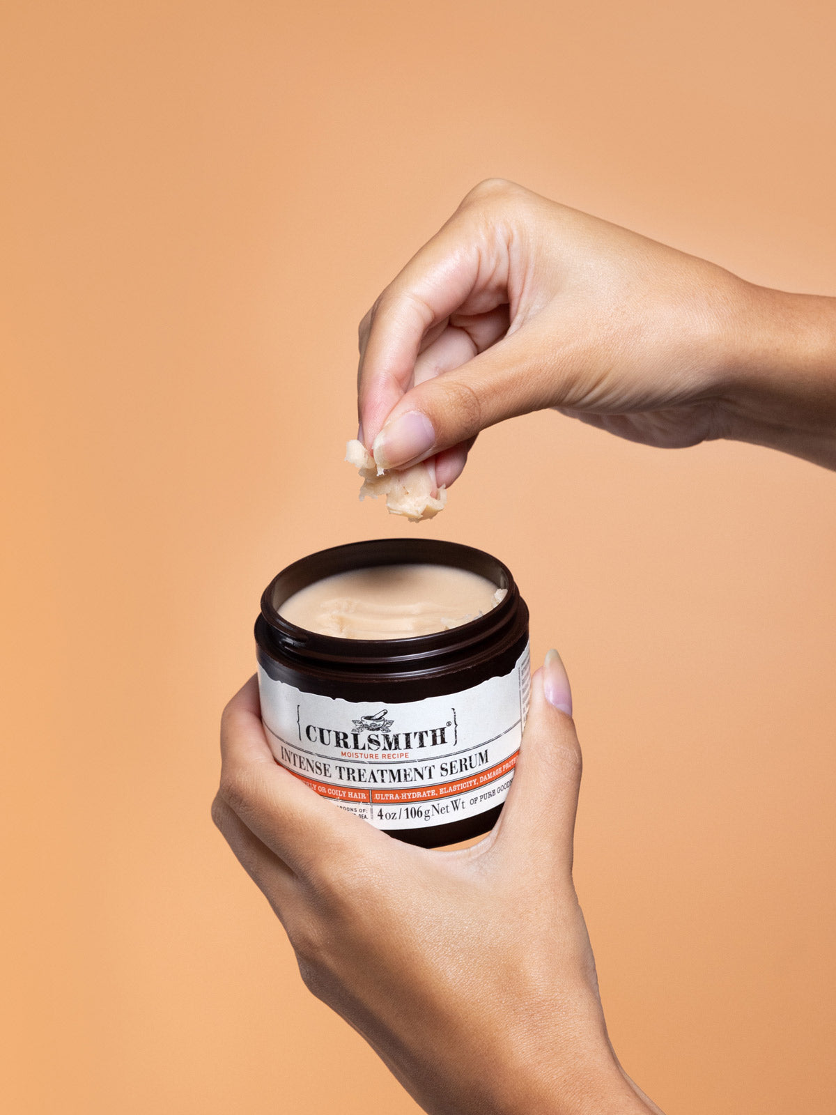 Curlsmith intense treatment serum jar with hand on an orange background