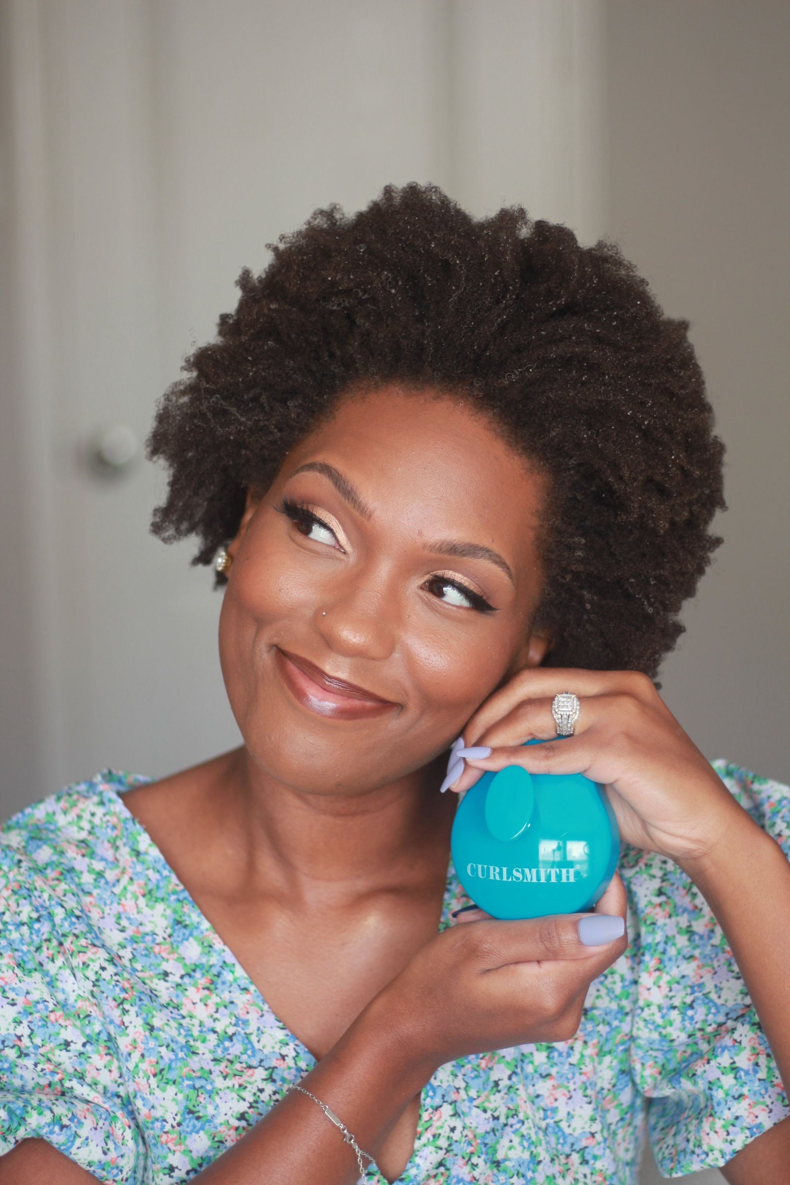 Woman holding a blue scalp massager with the brand name Curlsmith inscribed on it.