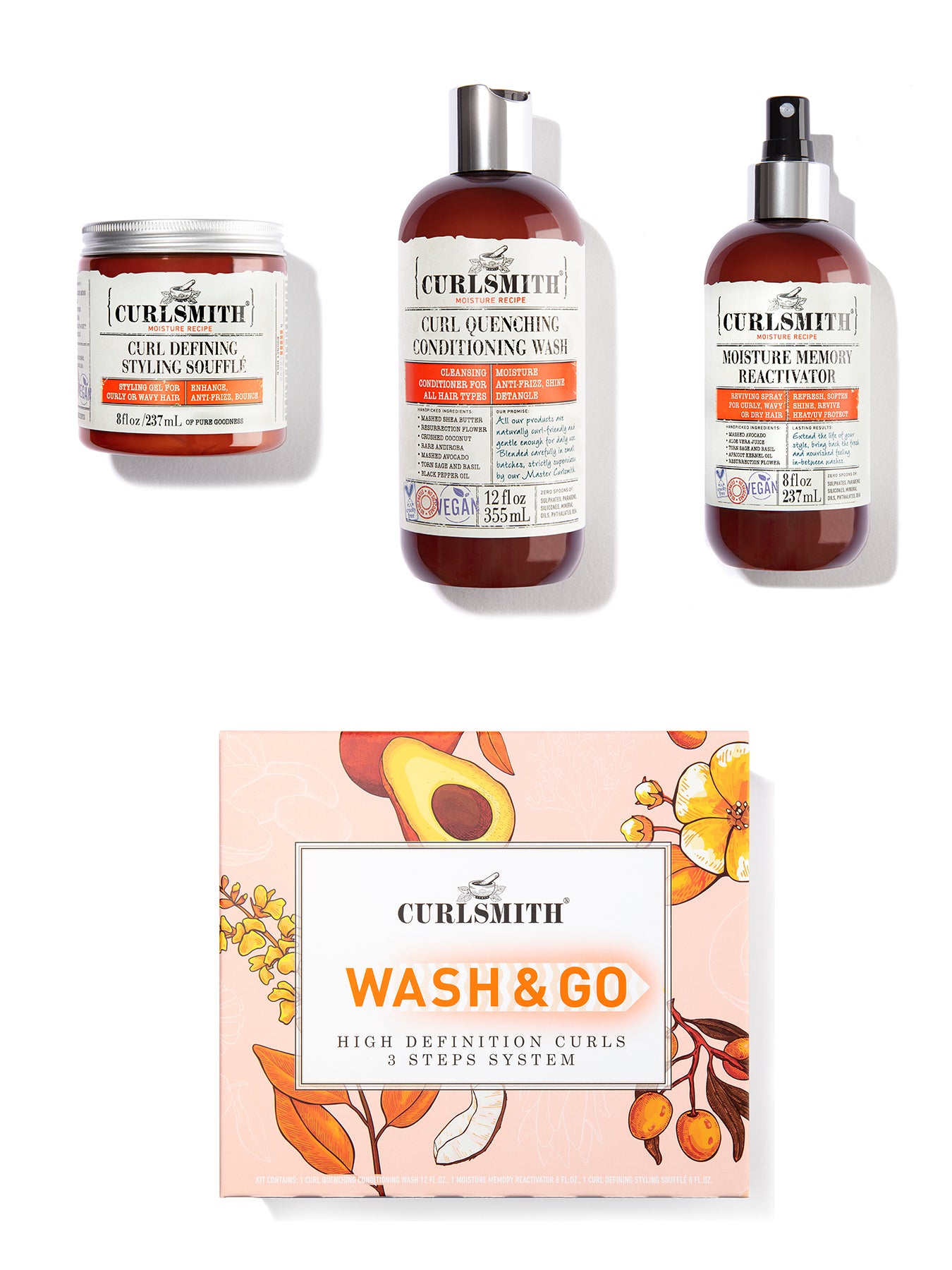 A set of hair care products from Curlsmith including a jar, bottle, and spray can with orange labels, along with a 'Wash & Go' kit box featuring floral and fruit illustrations.