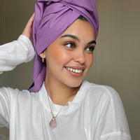 A person with smiling facial expression, wrapping a purple microfiber towel around their head.